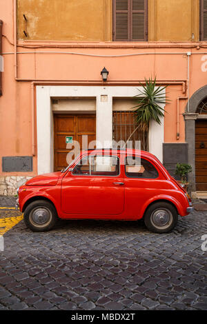 Ein alter roter Fiat 500 in einer gepflasterten Straße in Rom, Italien, außerhalb eines Gebäudes geparkt, das Werk ist nicht aus dem Schiebedach! Stockfoto