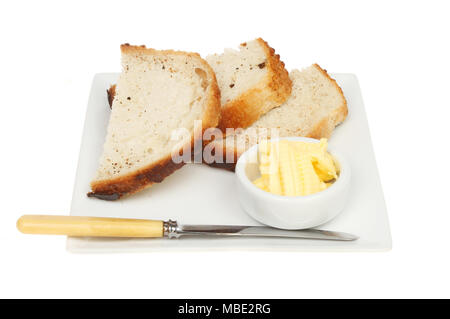 Scheiben knusprigem Brot auf eine quadratische Platte mit einem Messer und Butter in einem ramekin gegen Weiße isoliert Stockfoto
