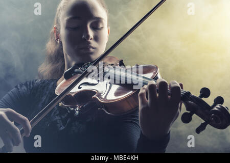 Frau Spielen der Violine vor einem dunklen Hintergrund. Nebel im Hintergrund. Studio shot Stockfoto