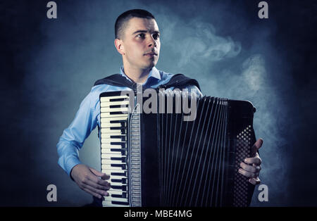 Musiker spielen auf dem Akkordeon vor einem schwarzen Hintergrund. Nebel im Hintergrund. Studio shot Stockfoto