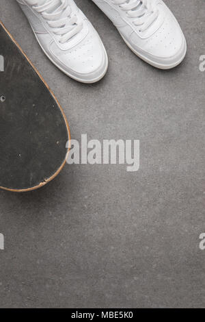 Blick von oben auf die weißen Turnschuhen und Skateboard auf grauem Asphalt Oberfläche Stockfoto