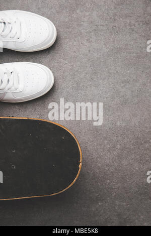 Blick von oben auf die weißen Turnschuhen und Skateboard auf Betonoberfläche Stockfoto