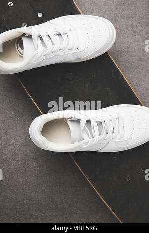 Blick von oben auf die weißen Turnschuhen auf Skateboard auf Betonoberfläche Stockfoto