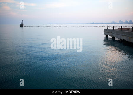 Michigan See bei Sonnenuntergang mit den rosa Himmel auf dem ruhigen Wasser und ein Steg reflektiert und unter Wasser Pier oder Wellenbrecher mit einem Marker Boje Stockfoto