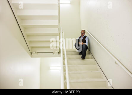 Asiatische Geschäftsmann sitzt in einem Treppenhaus der Arbeit auf einem Notebook. Stockfoto