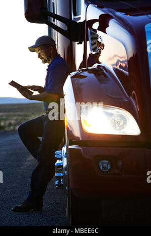 Lkw-Fahrer die Kontrolle sein Notebook Computer Anmelden beim Stehen neben der Kabine seiner Lkw nach Sonnenuntergang. Stockfoto