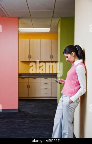 Kaukasische Geschäftsfrau texting und lehnte sich gegen eine bunte Wand in einem Büro. Stockfoto