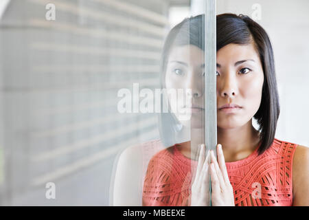 Eine asiatische Geschäftsfrau auf eine Glaswand in einem Büro Lobby reflektiert. Stockfoto