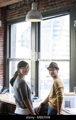 Asiatische Frau und Hispanic Mann zusammen Neben großen Fenstern in einer kreativen Büro. Stockfoto