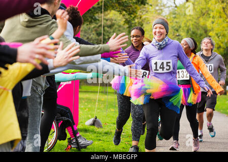 Begeisterte Läuferinnen mit tütü high-fiving Zuschauer am Spendenlauf in Park Stockfoto