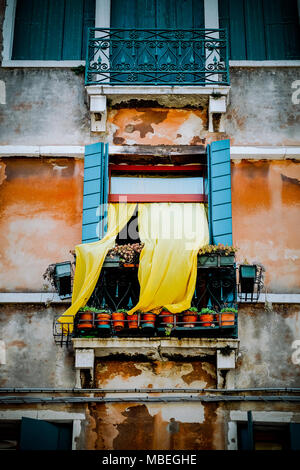 Eine gelbe Vorhang drapiert und in den Wind aus einer alten Fenster in Venedig Stockfoto