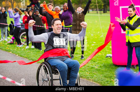 Begeisterte Menschen im Rollstuhl Überschreiten der Ziellinie an der Nächstenliebe Rennen in Park Stockfoto