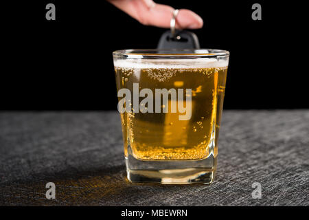Finger halten ein Auto Schlüssel hinter Tasse Bier Konzept des betrunkenen Fahrens Stockfoto