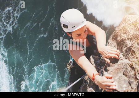 Bestimmt, fokussierte weiblichen Kletterer hängen von Rock über sonnige Ozean Stockfoto