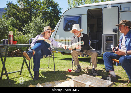 Active Senior Freunde lesen außerhalb Wohnmobil im sonnigen Sommer Campingplatz Stockfoto