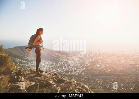 Weibliche Kletterer auf dem Hügel mit Blick auf die sonnige Stadt Stockfoto