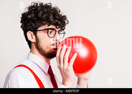 Portrait einer jungen gutaussehenden Mann in die Luft jagen einem roten Ballon in einem Studio. Close Up. Stockfoto