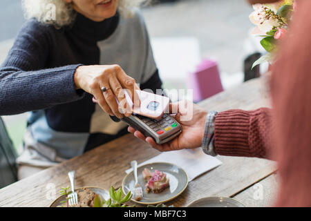 Frau mit smart phone über kontaktlose Zahlung im Cafe Stockfoto