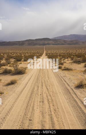 Lange Geraden Feldweg führt quer durch die Wüste und in die Berge von Wolken bedeckt. Stockfoto