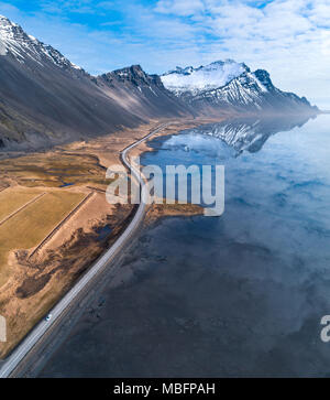 Hohen winkel Luftaufnahme von einer Straße vom Meer in Richtung Abstand mit Schnee Berge in Island im Frühjahr führende Stockfoto