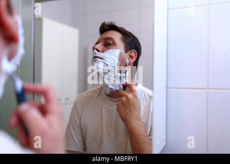 junger Mann mit Rasiermesser rasieren und Rasiercreme in Bad Stockfoto