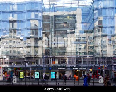 Gebäude in der Friedrichstraße, Berlin fast vollständig aus Glas, etwas wellig, Geschäfte und Menschen auf der gegenüberliegenden Seite der Straße. Stockfoto