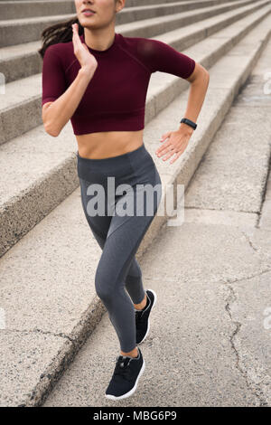 Sportliche brunette läuft neben Treppen in Fitness Kleidung, schwarze Turnschuhe und beobachten Stockfoto