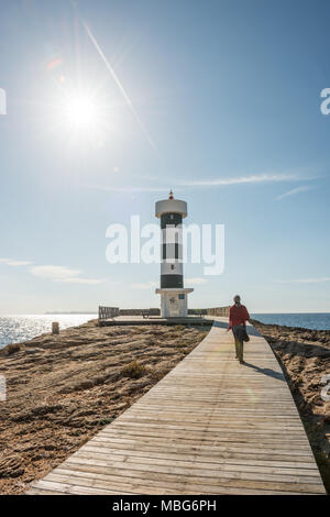 Eine junge Frau mit grauen Haaren und einem roten Schal Spaziergänge entlang der Promenade auf den Leuchtturm an der Küste in Colonia de Sant Jordi, Mallorca. Stockfoto