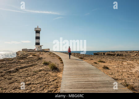 Eine junge Frau mit grauen Haaren und einem roten Schal Spaziergänge entlang der Promenade auf den Leuchtturm an der Küste in Colonia de Sant Jordi, Mallorca. Stockfoto