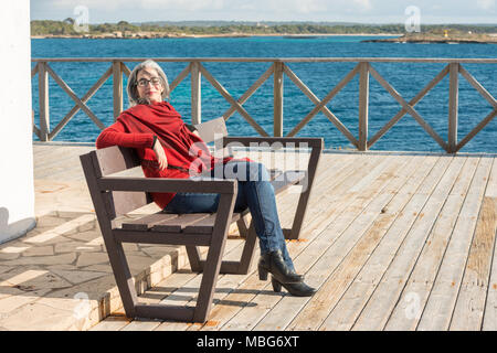 Eine junge Frau mit ergrauten Haare und ein rotes Halstuch, sitzen auf einer Bank in der Nähe von Colonia de Sant Jordi auf Mallorca, Spanien. Stockfoto