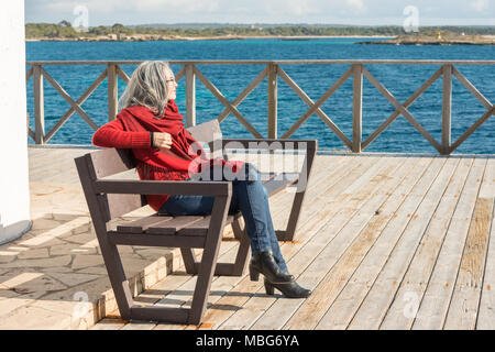 Eine junge Frau mit ergrauten Haare und ein rotes Halstuch, sitzen auf einer Bank in der Nähe von Colonia de Sant Jordi auf Mallorca, Spanien. Stockfoto