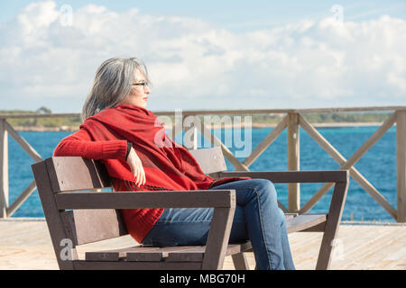 Eine junge Frau mit ergrauten Haare und ein rotes Halstuch, sitzen auf einer Bank in der Nähe von Colonia de Sant Jordi auf Mallorca, Spanien. Stockfoto