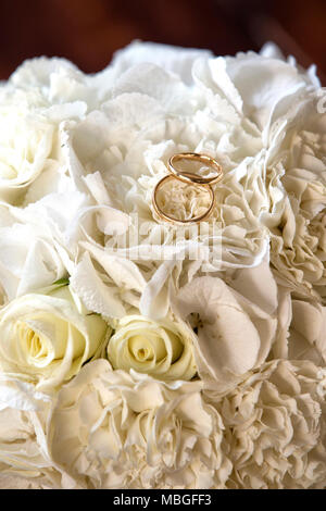 Vertikale Nahaufnahme von Hochzeit goldene Ringe an den wedding bouquet auf einem Holztisch Stockfoto
