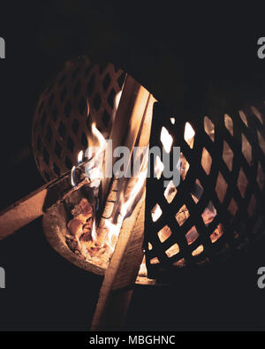 Das Verbrennen von Holz in runder Garten Brenner mit Grill Seitenwänden. Feuer, Flammen, gemütliche Nacht Atmosphäre in Garten, Outdoor. Stockfoto