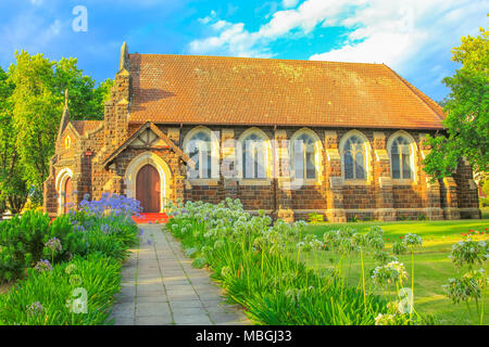 St. Georges anglikanische Kirche und blühenden Garten in Knysna, Stadt an der Garden Route in der Western Cape, Südafrika. Die historische Kirche, 1855 gebaut. Sonnenuntergang geschossen. Von der Seite. Stockfoto
