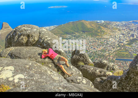 Junge Reisende liegen nach einer Wanderung auf den Tafelberg NP. Sportliche Frau mit Panoramablick auf Hafen Kapstadt und am Wasser von oben auf dem Tafelberg, Western Cape, Südafrika. Stockfoto