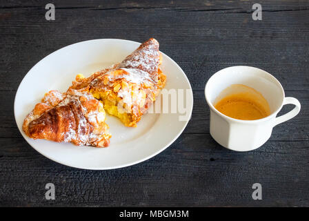 Mandel Croissant mit Tasse Espresso auf einem alten schwarzen Holztisch Stockfoto