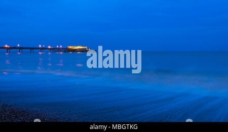 Wellen entlang viel Küste bei Dämmerung mit viel Pier beleuchtet im Hintergrund. Stockfoto