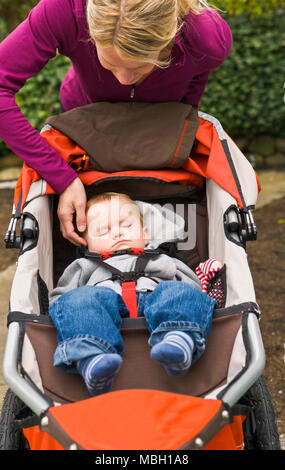 Eine Mutter sitzt auf der Treppe, die sich in Ihr Handy ein Baby schläft in einem laufenden stroller. Stockfoto