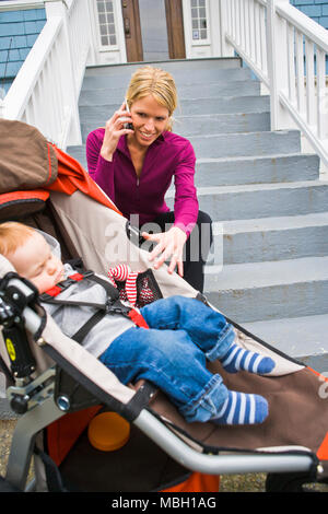 Eine Mutter sitzt auf der Treppe, die sich in Ihr Handy ein Baby schläft in einem laufenden stroller. Stockfoto