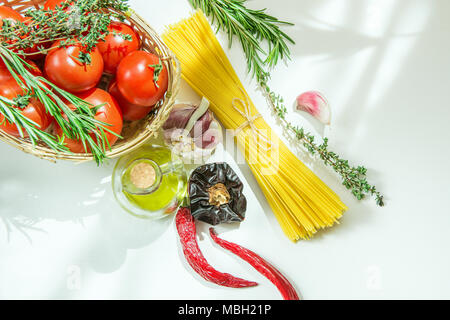 Reif Bio Tomaten Kräuter Rosmarin Thymian im Weidenkorb. Spaghetti Olivenöl in der Flasche Peperoni Knoblauch auf weißen Stein Beton Küchentisch. S Stockfoto