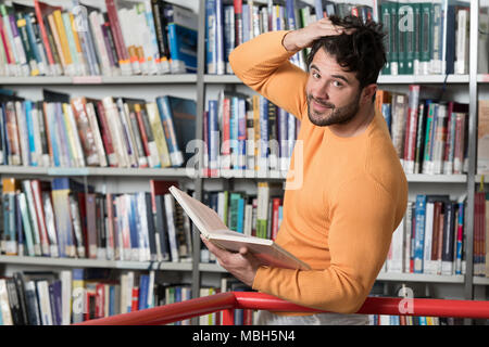 Stattlicher Mann mit dunklen Haaren steht in der Bibliothek - Studentische Vorbereitung Prüfung und Lehren in der Schule Bibliothek Stockfoto
