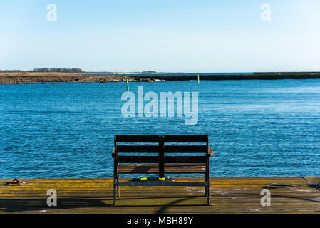 Leere Holzbank am Ende der Pier mit einem verschwommenen Blick auf Hafen- und coastland. Lage Gronhogen auf Oland, Schweden. Stockfoto