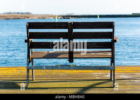 Leere Holzbank am Ende der Pier mit einem verschwommenen Blick auf Hafen- und coastland. Lage Gronhogen auf Oland, Schweden. Stockfoto