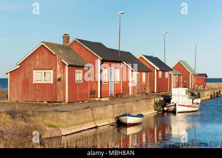 Gammalsby Hafen am östlichen Oland, Schweden. Kleine rote Holz- Angeln Kabinen in einer Reihe auf der Pier mit kleinen Booten dockside am Abend sunlig Stockfoto