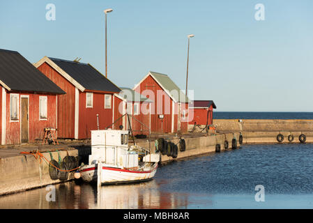 Gammalsby Hafen am östlichen Oland, Schweden. Kleine rote Holz- Angeln Kabinen in einer Reihe auf der Pier mit kleinen Booten dockside am Abend sunlig Stockfoto