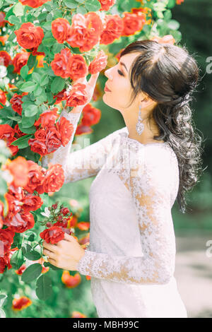 Die Seite Portrait von die schöne Braut berühren und riecht die roten Rosen. Stockfoto