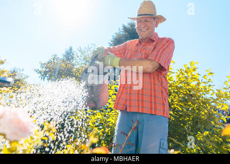 Active Senior mann Bewässerung von Pflanzen im Garten in einem ruhigen Tag Stockfoto