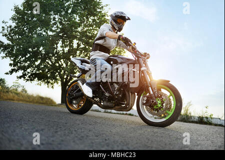 Ternopil, Ukraine - 28. August 2015: Foto von Biker, durch das Tragen von schützender helm sitzt auf seine bunte sport Motorrad stehen auf Sommer Straße, mit Glanz von Sonnenuntergang gefüllt. Stockfoto