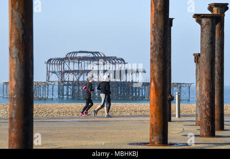 Brighton. 11. April 2018. UK Wetter: Läufer Vorbei an der verfallenen West Pier hinter dem Golden Spiral Artwork auf Brighton direkt am Meer an einem schönen sonnigen Morgen entlang der Südküste mit der Wettervorhersage gesehen bis in Großbritannien in den nächsten Tagen warm. Viele Läufer sind in der Ausbildung für den Brighton Marathon, der findet am kommenden Sonntag: Simon Dack/Alamy leben Nachrichten Stockfoto